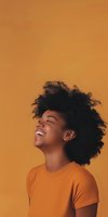 Young African American woman with natural afro hair laughing joyfully against orange background, wearing matching orange t-shirt, expressing genuine happiness and freedom.
