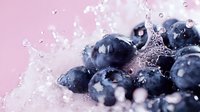 Fresh ripe blueberries with water splash and droplets on pink background. Macro shot of juicy berries with dynamic water motion for healthy food concept.