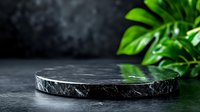 Black marble podium with green tropical leaves on dark background for luxury product display and branding presentations.