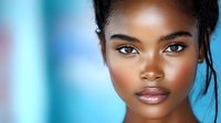 Young African American woman with flawless glowing skin and natural makeup against blurred blue background, expressing confidence and grace in close-up portrait.