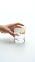 Hand holding glass of fresh water with lemon slice and ice cubes on white background, isolated for beverage, wellness, hydration and healthy lifestyle design use.