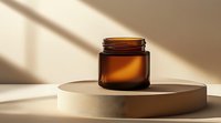 Empty amber glass cosmetic jar on beige podium with dramatic diagonal shadow and sunlight, minimalist luxury beauty product presentation.
