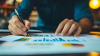 Close up of hands analyzing financial charts and graphs on blue paper with pen, warm lighting creates professional business atmosphere for financial reports.