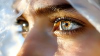 Striking close-up of bright blue eyes with golden sunlight creating dramatic shadows and highlights. Natural eye makeup enhances the intense gaze and ethereal mood.