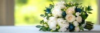 Wedding bouquet with white roses and peonies decorated with blue thistle flowers and green eucalyptus leaves on bright background for bridal ceremony.