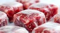 Fresh raw beef cubes wrapped in plastic film with selective focus. Marbled meat texture shows premium quality cuts ready for cooking or freezing.
