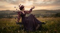 Surreal artistic portrait of woman in flowing dark dress dissolving into butterflies at golden sunset in wildflower meadow with dramatic sky and rolling hills.