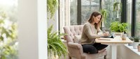 Young professional woman working on laptop in modern bright office space with plants and natural light for remote work and productivity concepts.
