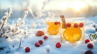 Hot winter drink with orange slices, cinnamon sticks and fresh cranberries in glass cups on snowy background with sunlight and frost covered branches.