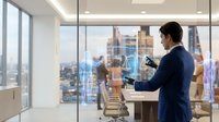 Professional businesswoman using tablet with holographic data visualization in modern corporate office with city skyline view during daytime meeting.