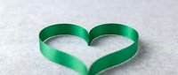 Green ribbon heart shape on white background symbolizing love, care and environmental awareness for romantic and eco-friendly design projects.