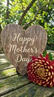 Rustic wooden heart sign with Happy Mother's Day text and burgundy dahlia flower on weathered wood table outdoors for greeting card and celebration design.