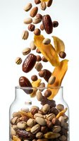 Assorted nuts and dried fruits cascading into glass jar against white background, featuring almonds, pistachios, dates, and mango slices for healthy snacking, nutrition, and food photography.