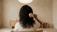 Young African American woman with curly hair combing her natural textured hair in modern bedroom interior for haircare and beauty routine.