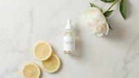 Citrus-infused skincare serum bottle displayed on marble surface with fresh lemon slices and white peony flower, ideal for beauty and wellness product marketing.