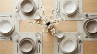 Elegant dining table setting for six with neutral tableware and spring cherry blossom centerpiece on wooden surface ready for dinner party.