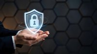 Businessman holding glowing cybersecurity shield with padlock icon over dark hexagonal background representing data protection and digital security solutions.