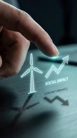 Businessman pointing at holographic wind turbine with upward arrow and social impact text on digital surface, renewable energy growth concept.