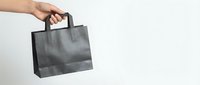 Hand holding black paper shopping bag against white background for retail and commercial use.