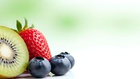 Fresh mixed berries and kiwi fruit arrangement on clean white surface with soft green bokeh background for healthy eating and nutrition concepts.