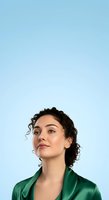 Young woman with curly dark hair and olive complexion wearing emerald satin shirt against clear blue background, looking upward thoughtfully for portrait and lifestyle use.