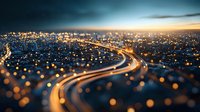 Aerial view of illuminated highway winding through night city with glowing lights creating bokeh effect. Urban landscape with dramatic sky and light trails from traffic.