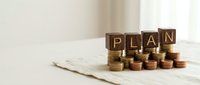 Financial planning concept with wooden letter blocks spelling PLAN on stacked coins representing savings strategy and budget management for future goals.