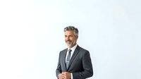 Middle-aged man with gray hair and beard, Caucasian ethnicity, wearing dark business suit and tie. Professional businessman isolated on white background for corporate portraits and business applications.