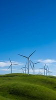Wind turbines on rolling green hills under clear blue sky with white clouds, generating renewable energy for sustainable power production and environmental conservation.