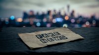 Fake news newspaper headline on wooden surface with blurred city lights background at dusk. Media misinformation and journalism concept for editorial use.