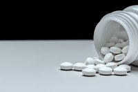 White pharmaceutical pills spilling from prescription bottle on gray surface against black background, dramatic lighting highlights medical concept.