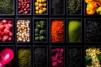 Colorful collection of spices, dried flowers, and tea ingredients in black compartment boxes, creating vibrant contrast and texture for culinary and wellness concepts.