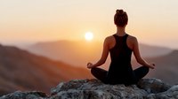 Woman meditating in lotus pose on mountain rock during golden sunset with peaceful valley landscape background for wellness and mindfulness concepts.