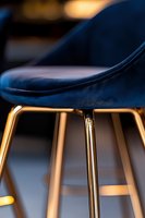 Modern navy blue velvet bar stool with luxurious gold metal legs close-up. Elegant furniture detail highlighting contemporary design and premium materials.