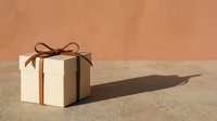 Elegant gift box with brown ribbon bow on warm beige background casting soft shadow for holiday celebrations and special occasions.