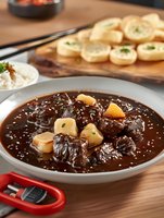 Tender beef bourguignon with potatoes in rich brown sauce, served with rice and garlic bread on wooden table, close up view of traditional French cuisine.