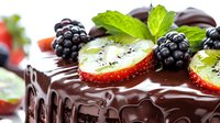 Dark chocolate cake decorated with fresh blackberries, sliced kiwi, and mint leaves on top, melted ganache dripping down sides creates luxurious dessert presentation.