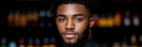 Young African American man with beard and curly hair in black clothing against blurred city lights background at night for lifestyle and portrait concepts.