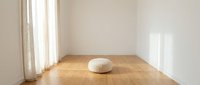 Minimalist meditation room with wooden floor and white cushion pillow in bright natural light from window creating peaceful zen atmosphere for yoga practice.