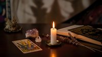 Mystical tarot cards spread on wooden table with burning candle, crystals and dried herbs creating atmospheric fortune telling scene for spiritual guidance.