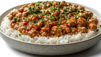 Spicy minced meat curry served on steamed white rice in ceramic bowl, garnished with fresh chopped herbs and chili peppers, close up view of Asian cuisine.