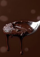 Rich melted chocolate dripping from a silver spoon against a dark brown background with soft bokeh effect.