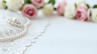 Elegant wedding background with white lace, pearl necklace and soft pink roses on white surface for bridal invitations and romantic designs.