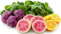 Fresh purple cauliflower, watermelon radish slices, oranges and green spinach leaves arranged on white background, healthy organic produce composition.