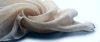 Soft beige fabric draped elegantly with flowing folds and gentle curves on white background. Luxurious textile material for fashion design and home decor projects.