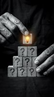 Elderly hands placing glowing lightbulb block atop pyramid of wooden question mark cubes representing problem solving and innovative thinking.