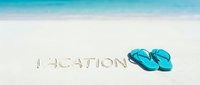 Vacation written in sand on a tropical beach with turquoise flip flops, ocean waves in background, summer holiday concept.