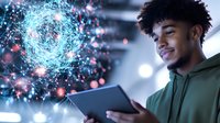Young African American man in green hoodie using digital tablet with glowing network visualization, artificial intelligence concept floating beside him in blue and pink.
