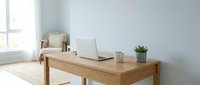 Modern minimalist home office workspace with wooden desk, laptop computer and small potted plant in bright natural light for remote work productivity.