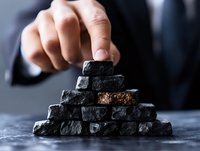 Male hand stacking rough black coal pieces in pyramid shape on dark background, demonstrating energy resources and fossil fuel industry concept.